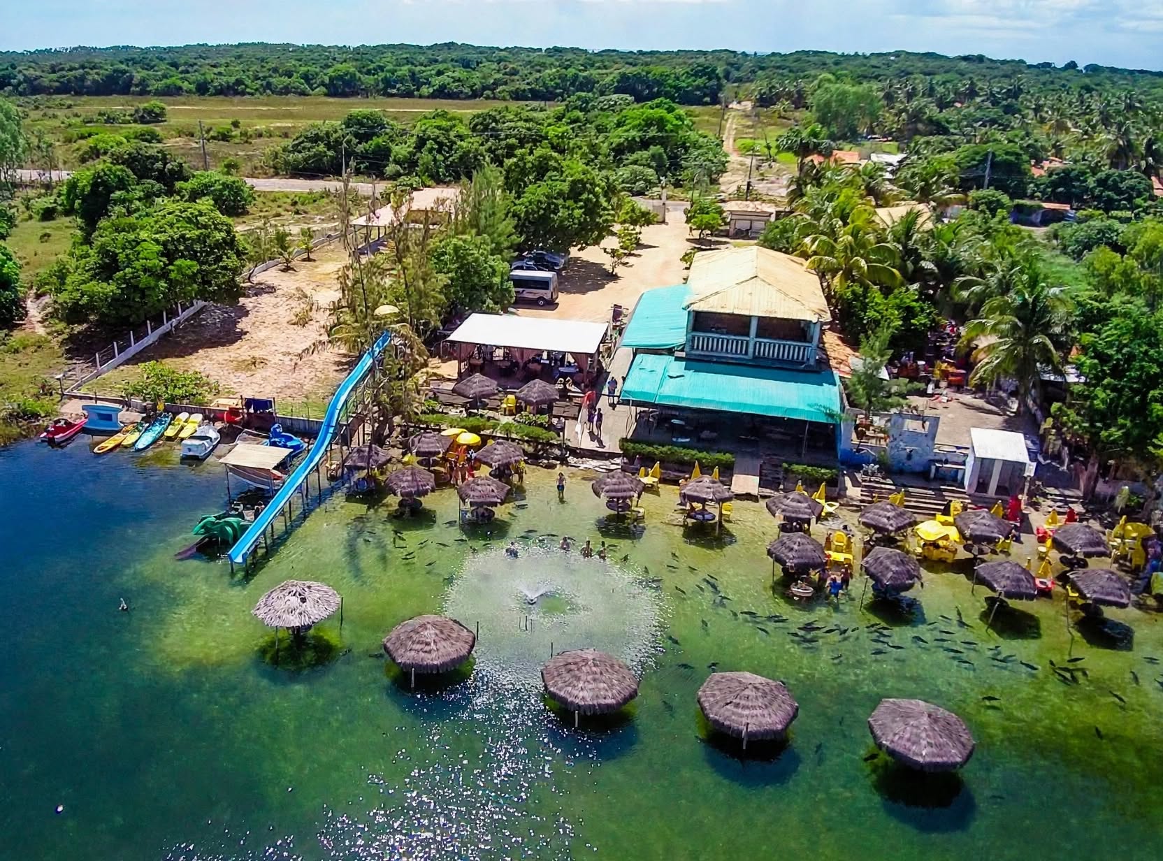 Vista aérea da Lagoa dos Tambaquis no Paraíso dos Tambaquis em Estância, Sergipe, com quiosques de palha, tobogã aquático, guarda-sóis e banhistas em águas cristalinas